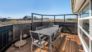 A wooden deck with a table and chairs, overlooking a grassy area with buildings in the background. - 4 Star Holiday Home in Lokken (Lokken)