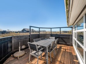 A wooden deck with a table and chairs, overlooking a grassy area with buildings in the background. - 4 Star Holiday Home in Lokken (Lokken)