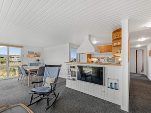 A modern interior with a dining area, a TV, and a kitchen with wooden cabinets. - 4 Star Holiday Home in Lokken (Lokken)