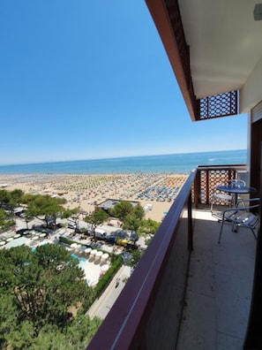 A balcony with a view of a beach, outdoor seating, and a clear sky. - Seaside Escape for Perfect Vacations (Lignano Sabbiadoro)