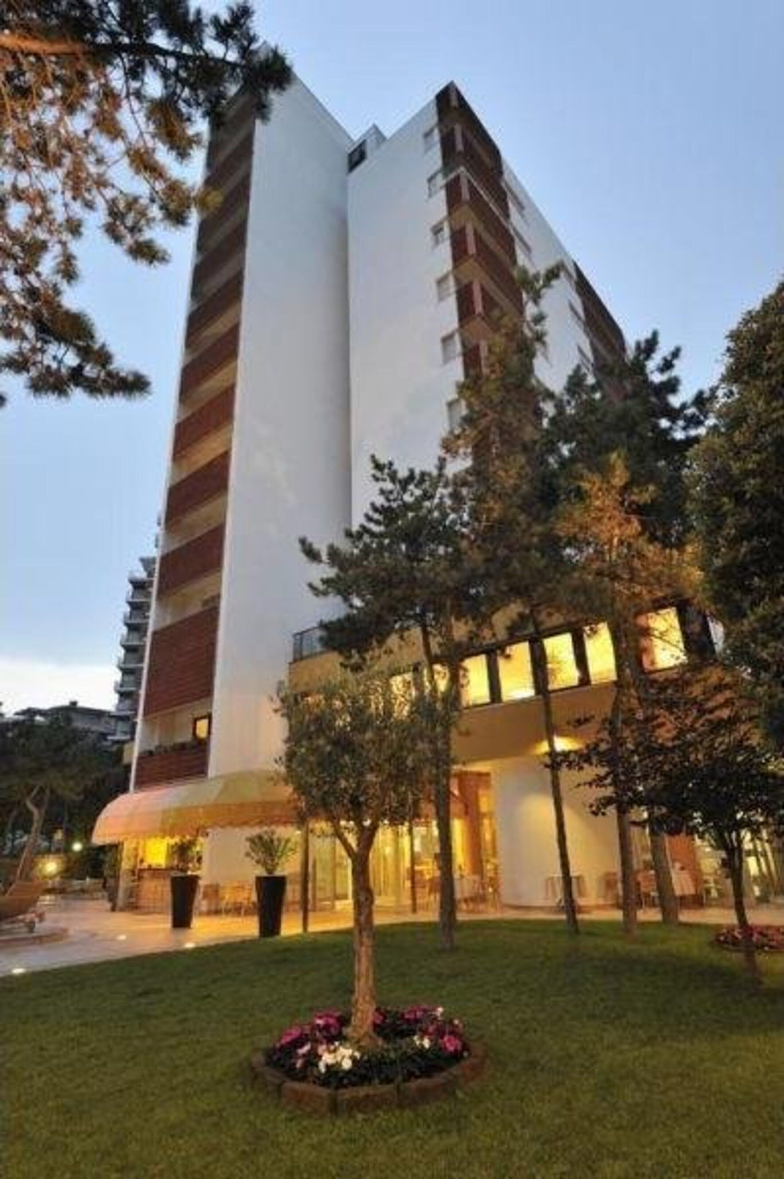A modern hotel with a multi-story structure, a well-maintained lawn, and a tree in the foreground.