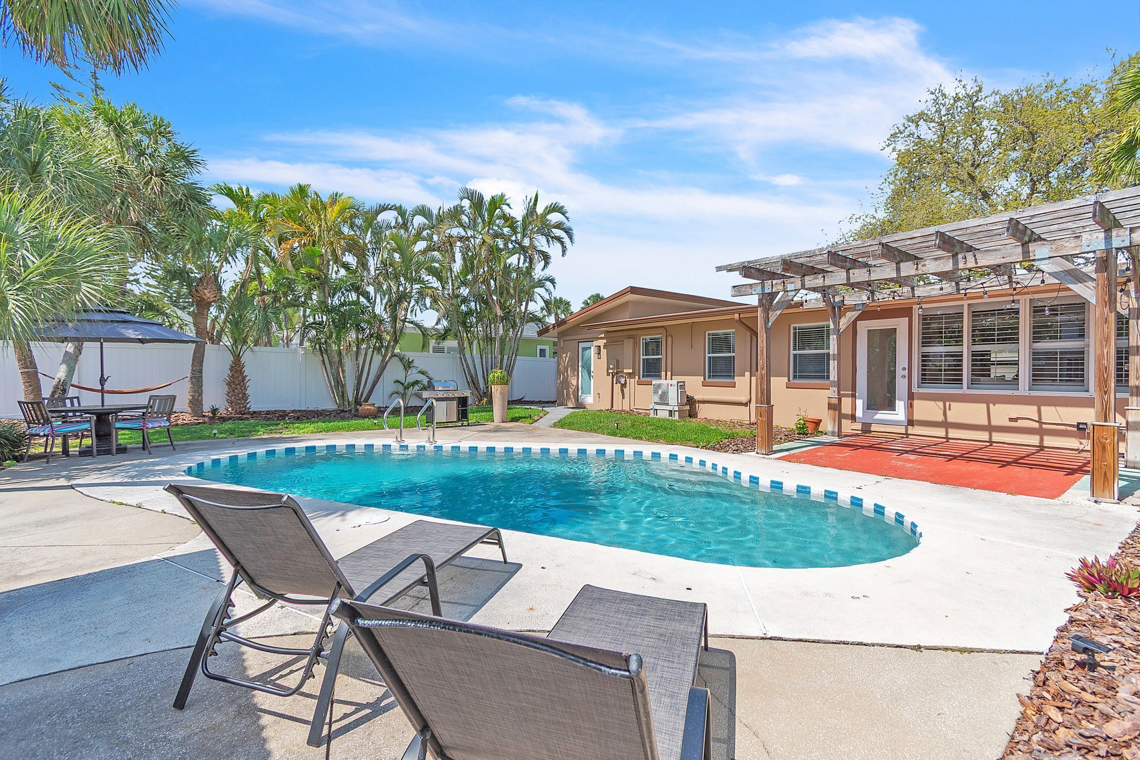 A swimming pool with lounge chairs, a pergola, and palm trees.