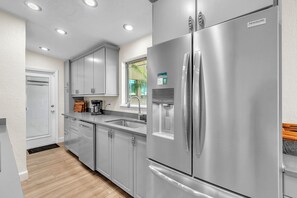 Une cuisine moderne dotée d’appareils électroménagers en acier inoxydable, d’une fenêtre offrant une belle vue et d’une porte donnant sur une autre pièce.