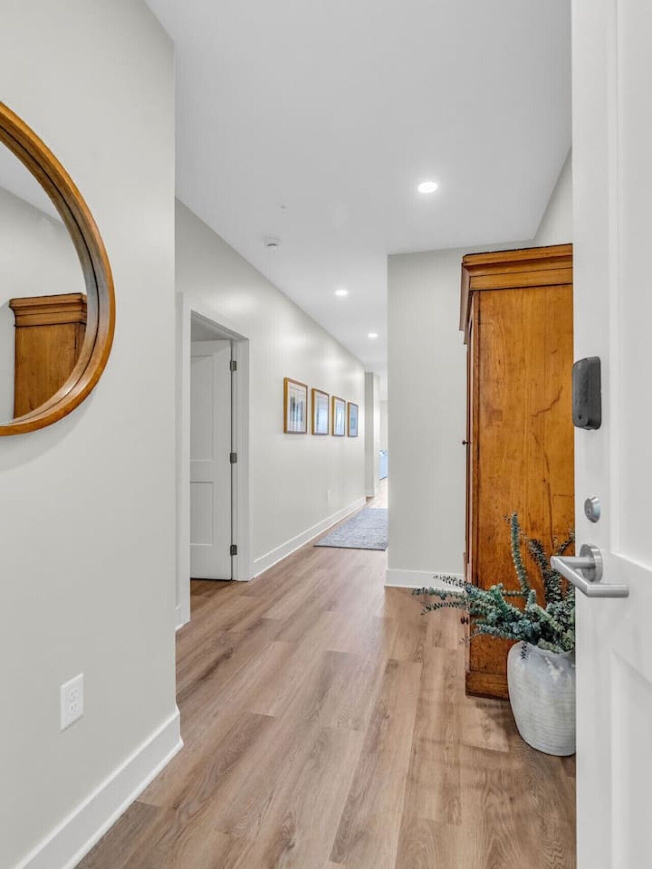 A hallway with wooden flooring, white walls, and a wooden door with a modern handle.