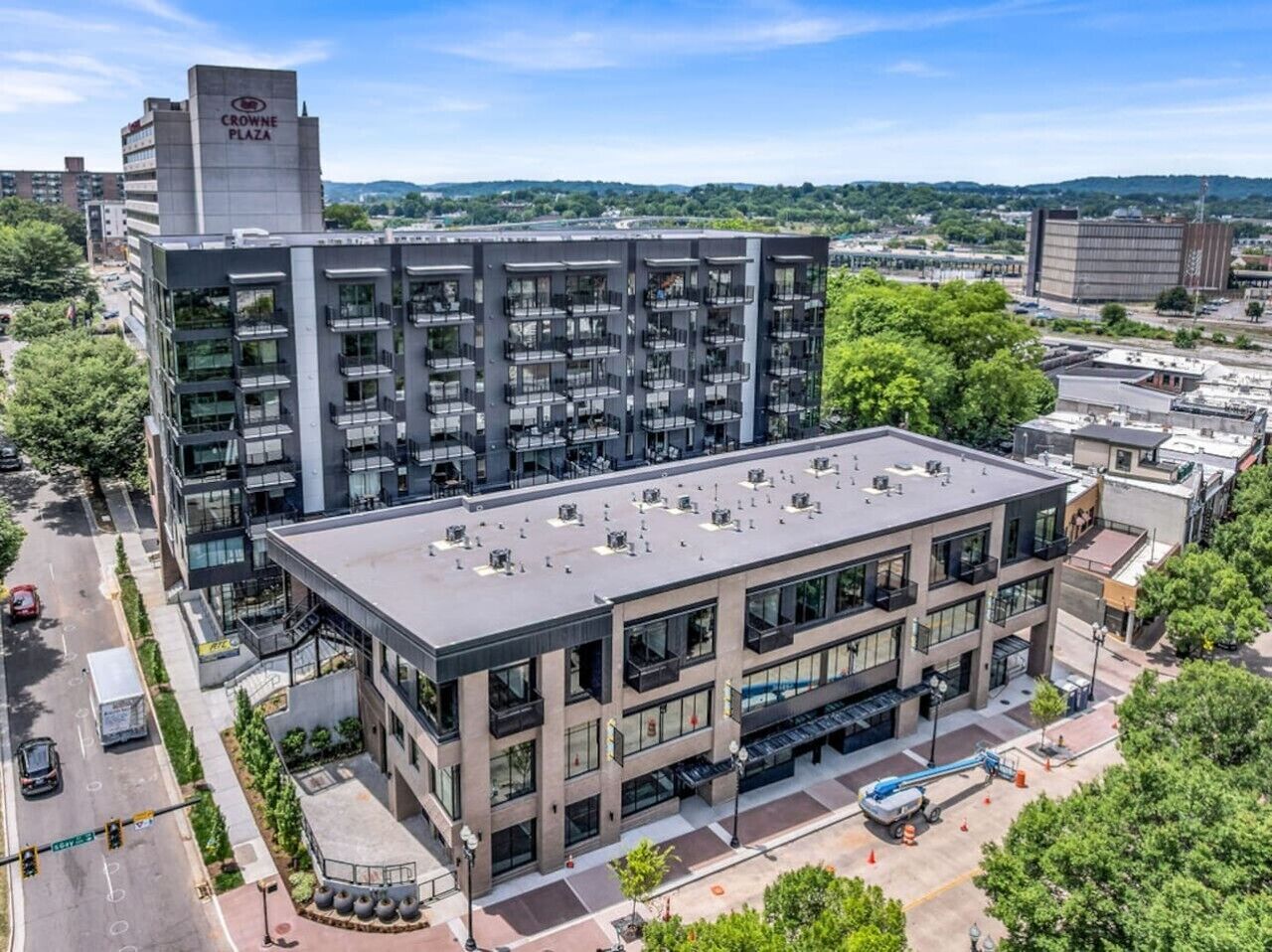 A multi-story building with a flat roof, large windows, and a parking area in front.