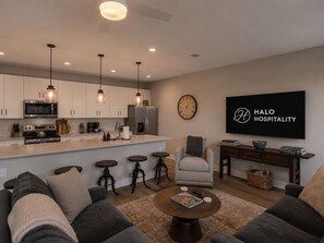 A modern living room with a sofa, coffee table, and a TV displaying 'HALO HOSPITALITY'. - Lone Tree Pass | King + Queen | Balcony + Parking (Knoxville)