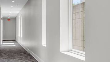 A corridor with a patterned carpet, recessed lighting, and a window with a view of a building.