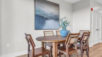 A dining area with a round wooden table and six chairs, a large abstract painting on the wall, and a potted plant.