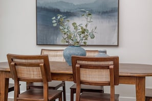 A dining table with two wooden chairs, a vase with green foliage, and a painting of a landscape. - Lone Tree Pass | King + Queen | Balcony + Parking (Knoxville)
