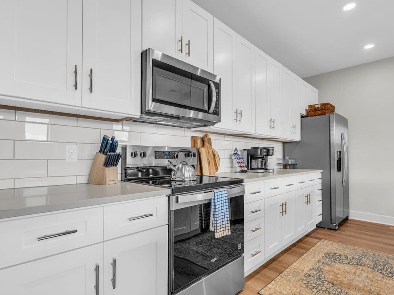A modern kitchen with white cabinets, stainless steel appliances, and a wooden floor.