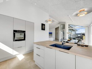 A modern kitchen with a built-in oven, a sink, and a dining area with a view. - 4 Star Holiday Home in Lokken (Lokken)