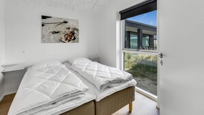 Een moderne slaapkamer met een groot bed, een plafondlamp, een raam met uitzicht op de omgeving, en een abstract schilderij aan de muur.