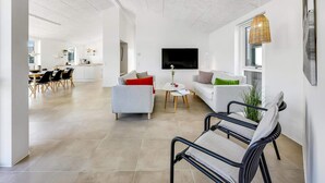 Een moderne woonruimte met een eethoek, een zithoek en een aan de muur bevestigde televisie.