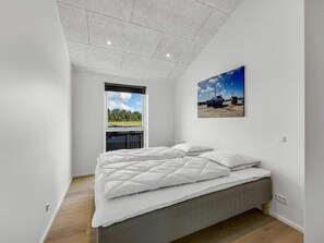 A bedroom with a bed, a window, and a painting of boats on a beach. - 4 Star Holiday Home in Lokken (Lokken)