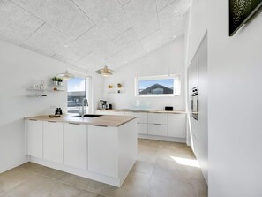 A modern kitchen with a central island, white cabinetry, and a view of a building outside. - 4 Star Holiday Home in Lokken (Lokken)