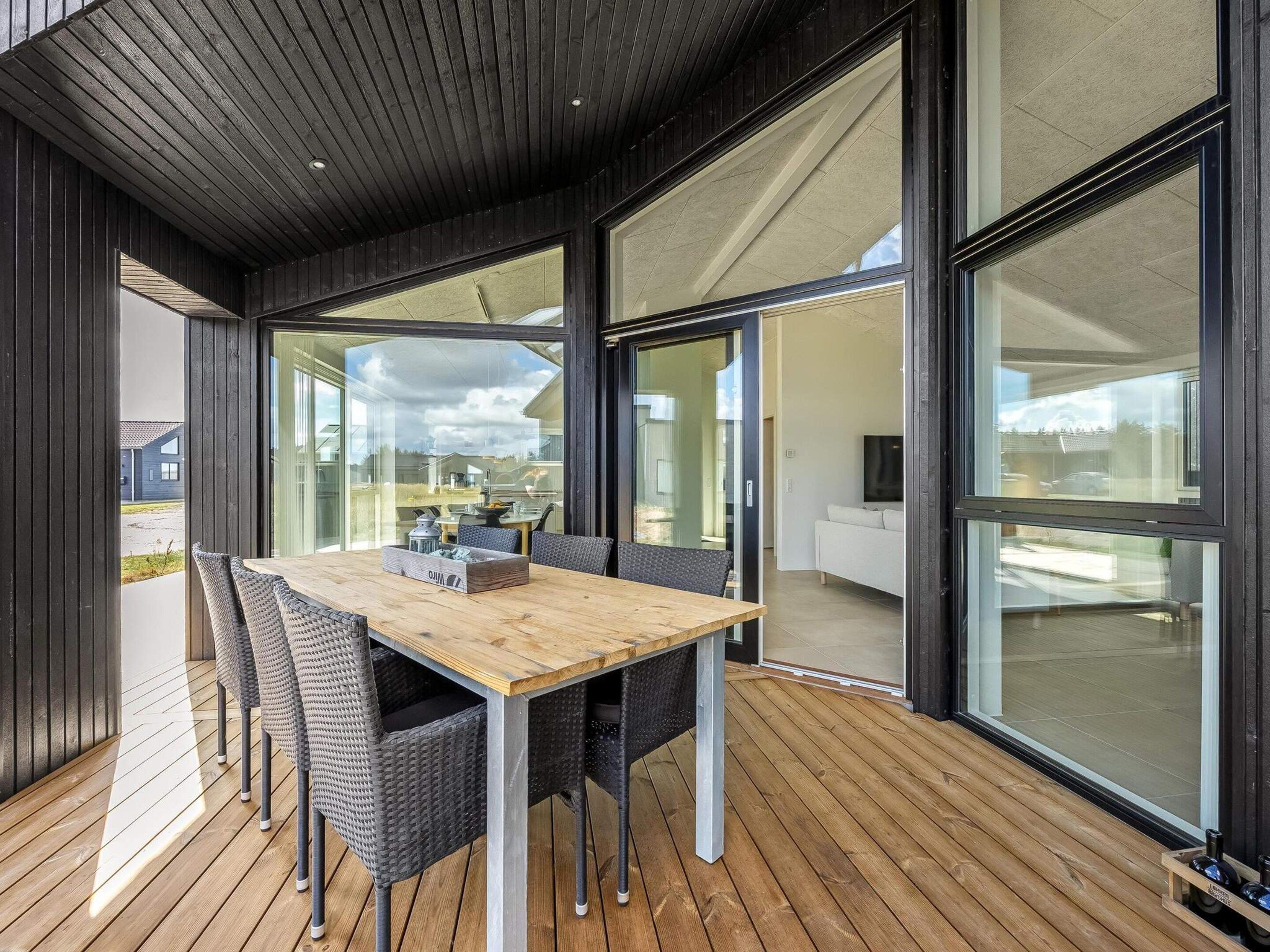 Een modern interieur met een houten terras, een eettafel met stoelen en grote ramen met uitzicht op de omgeving.