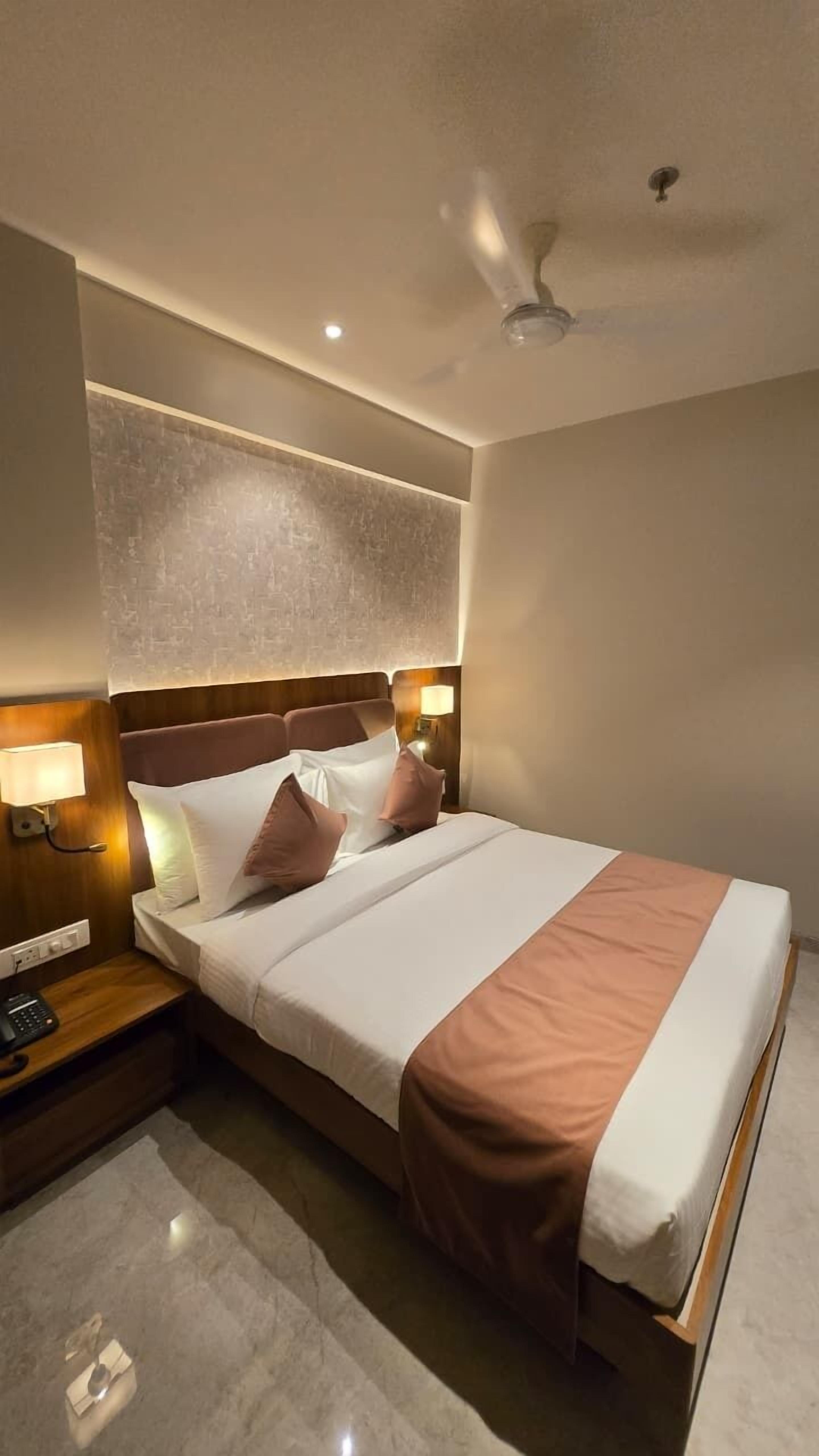A hotel room with a bed, bedside lamps, a ceiling fan, and a textured wall.