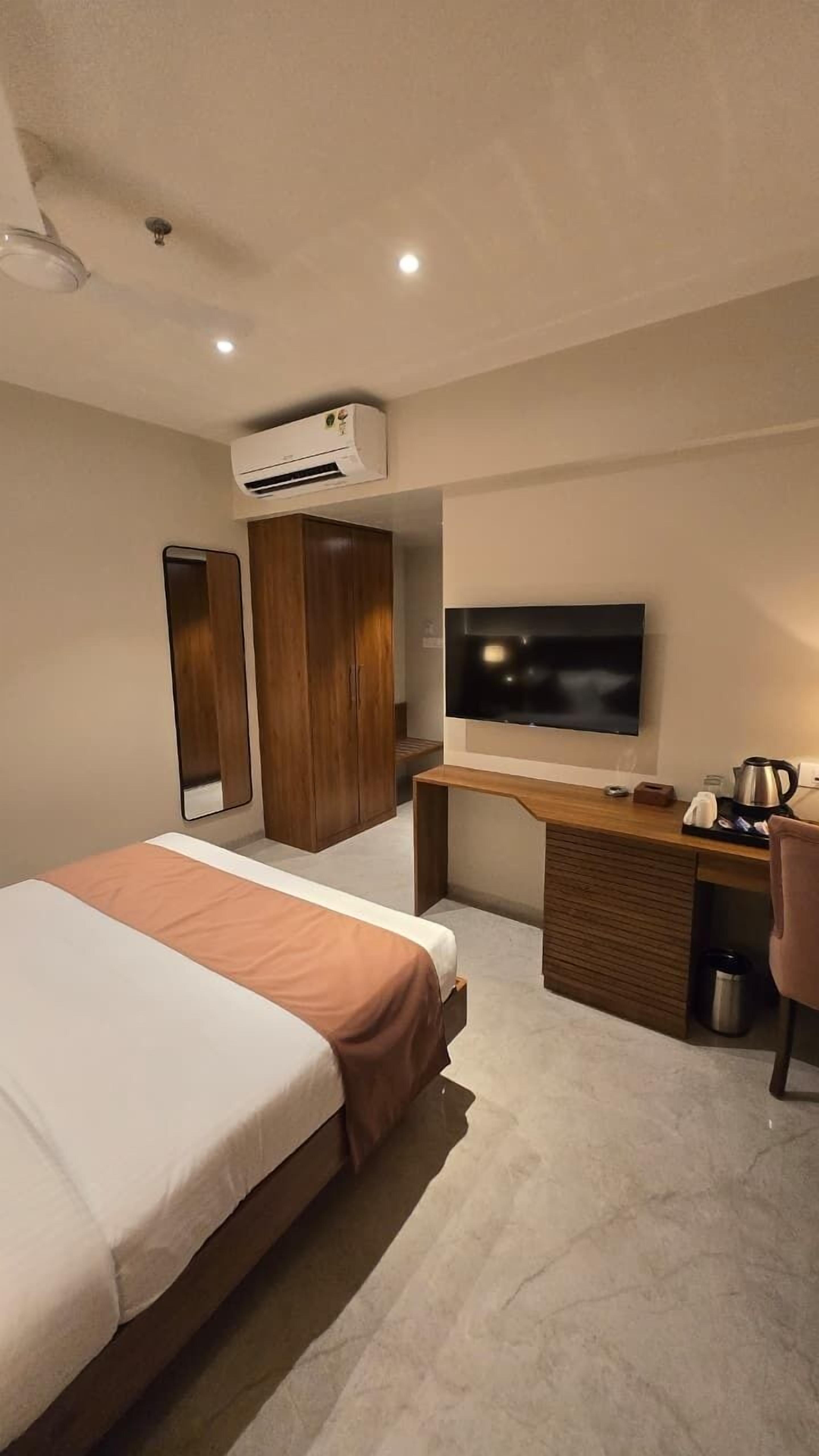 Een moderne hotelkamer met een bed, een bureau met een flatscreen-tv, een airconditioning en een houten garderobe.