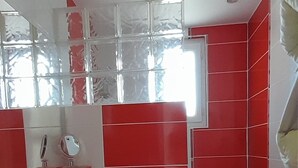 Eine kleine Küche mit weißen Arbeitsplatten, roten Schränken und einem Fenster über der Spüle.