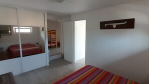 Ein Schlafzimmer mit Bett, Kleiderschrank, Spiegel und einer Tür zu einem weiteren Raum.