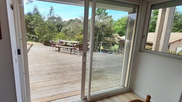 Blick durch eine Glasschiebetür auf eine Terrassenanlage mit Tisch und Stühlen.