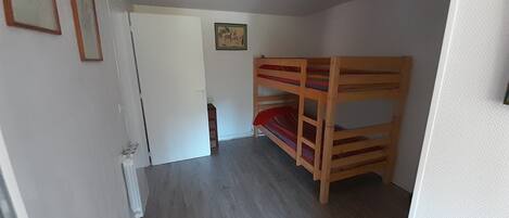 Une pièce avec un lit superposé, une porte, un radiateur et un tableau encadré au mur.