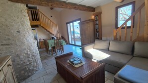 A spacious living area with a stone wall, wooden staircase, and a sofa. - Le Puits des Oliviers (Puimoisson)