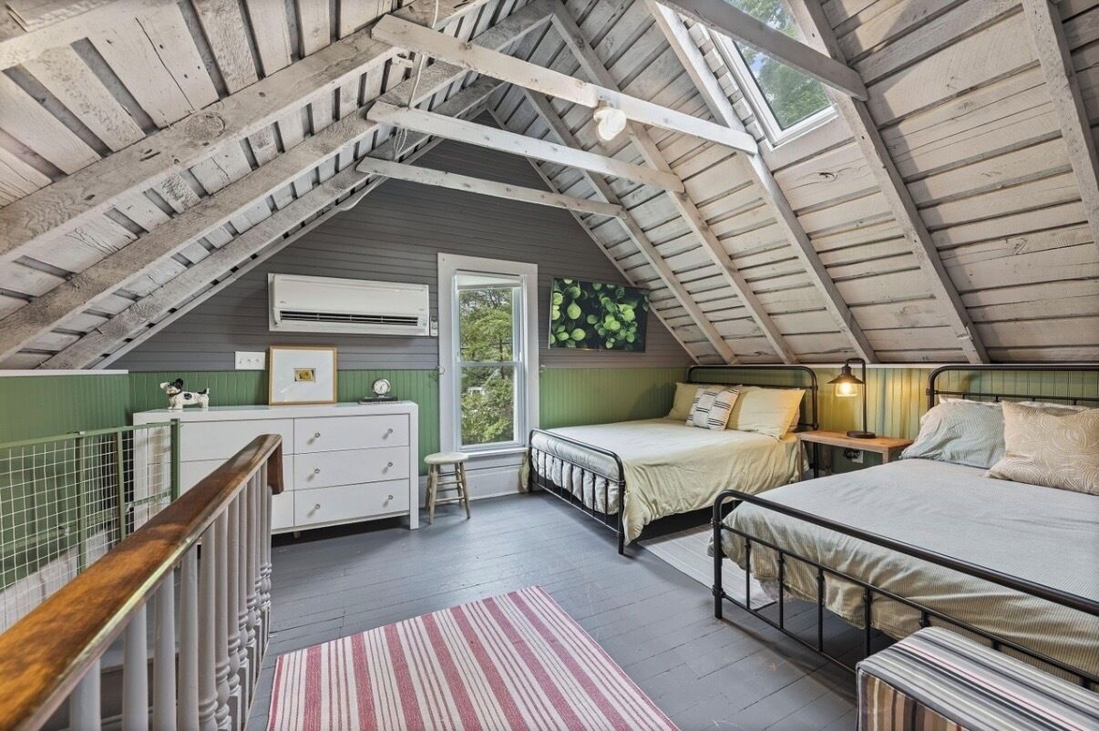 A loft bedroom with a sloped ceiling, a bed, a desk, and a window.