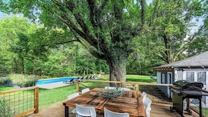 A wooden deck with a table and chairs, a barbecue grill, and a swimming pool in the background. - The Nordic cottage, huge modern pool, hot tub. (Union Pier)