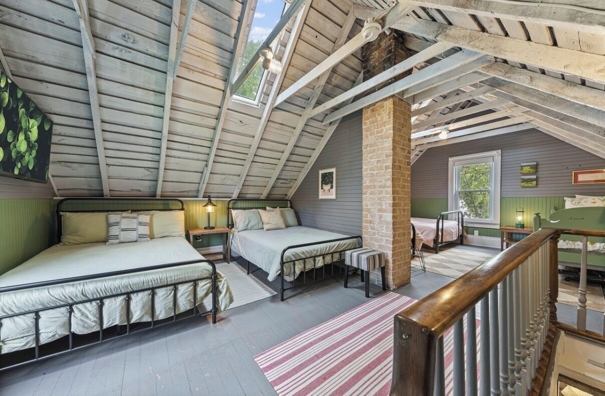 A loft bedroom with a sloped ceiling, two beds, a brick column, and a view of the outdoors.