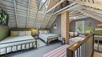 A loft bedroom with a sloped ceiling, two beds, a brick column, and a view of the outdoors.