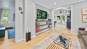 A modern living room with a wooden coffee table, bookshelves, and a large green artwork on the wall. - The Nordic cottage, huge modern pool, hot tub. (Union Pier)