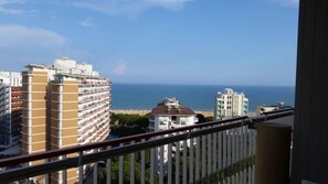 Ein Hochhaus mit mehreren Balkonen, Blick auf das Meer und Wohnhäuser im Hintergrund.