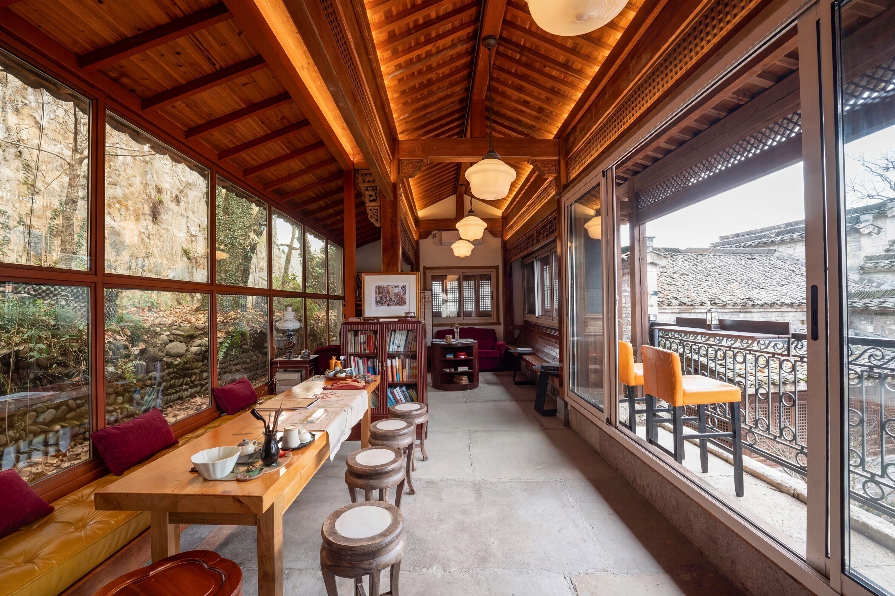A wooden interior with a long table, multiple stools, and a balcony with chairs.