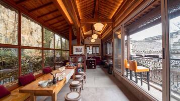 A wooden interior with a long table, multiple stools, and a balcony with chairs.