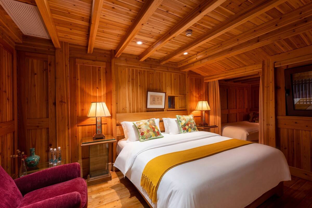 Una habitación con paneles de madera, una cama, dos lámparas, una silla y una pequeña mesa con un florero.