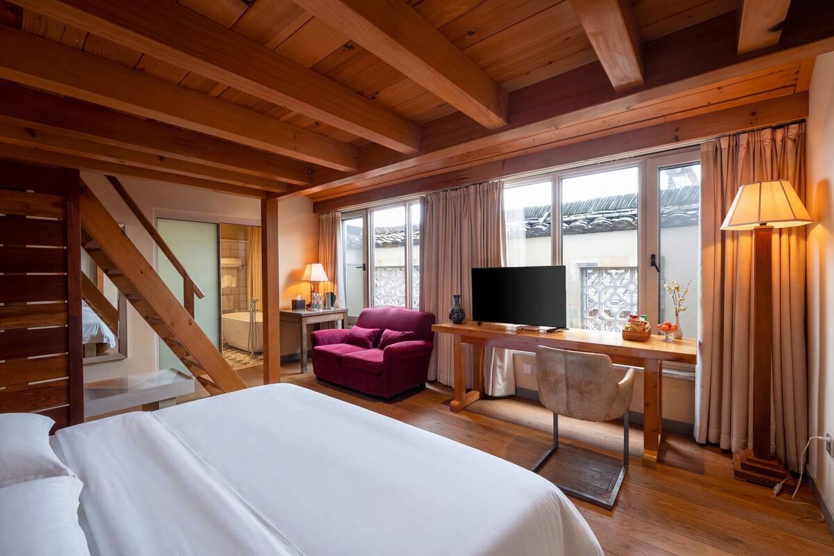 Habitación de hotel con cama, escritorio con computadora, televisor, sofá y escalera.