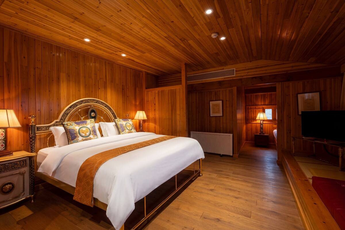 Un dormitorio con paneles de madera, una cama grande, lámparas de noche, un radiador y un televisor.
