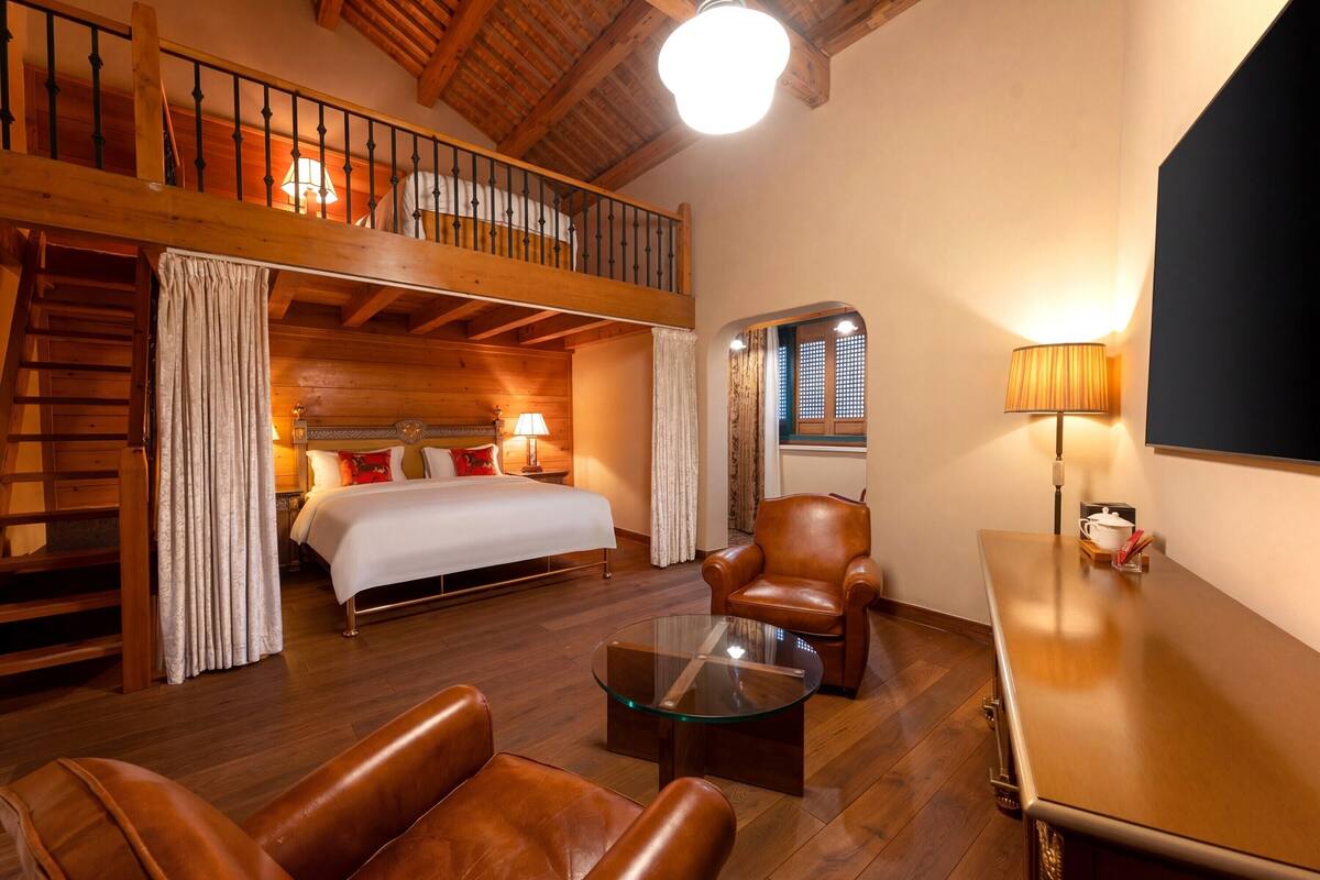 Una habitación con cama tipo litera, una mesa de centro de vidrio, sillones de cuero y un escritorio de madera.