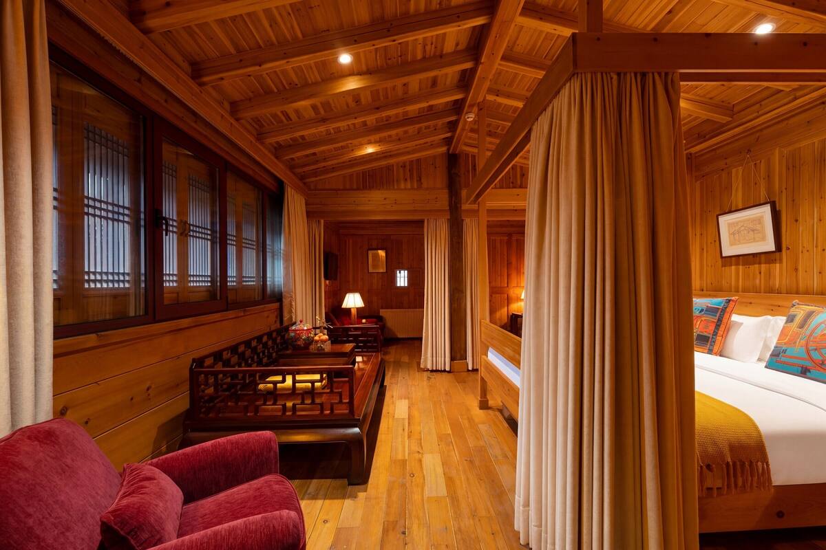 Un interior de madera con una cama, un espacio para sentarse y vistas a través de una ventana.