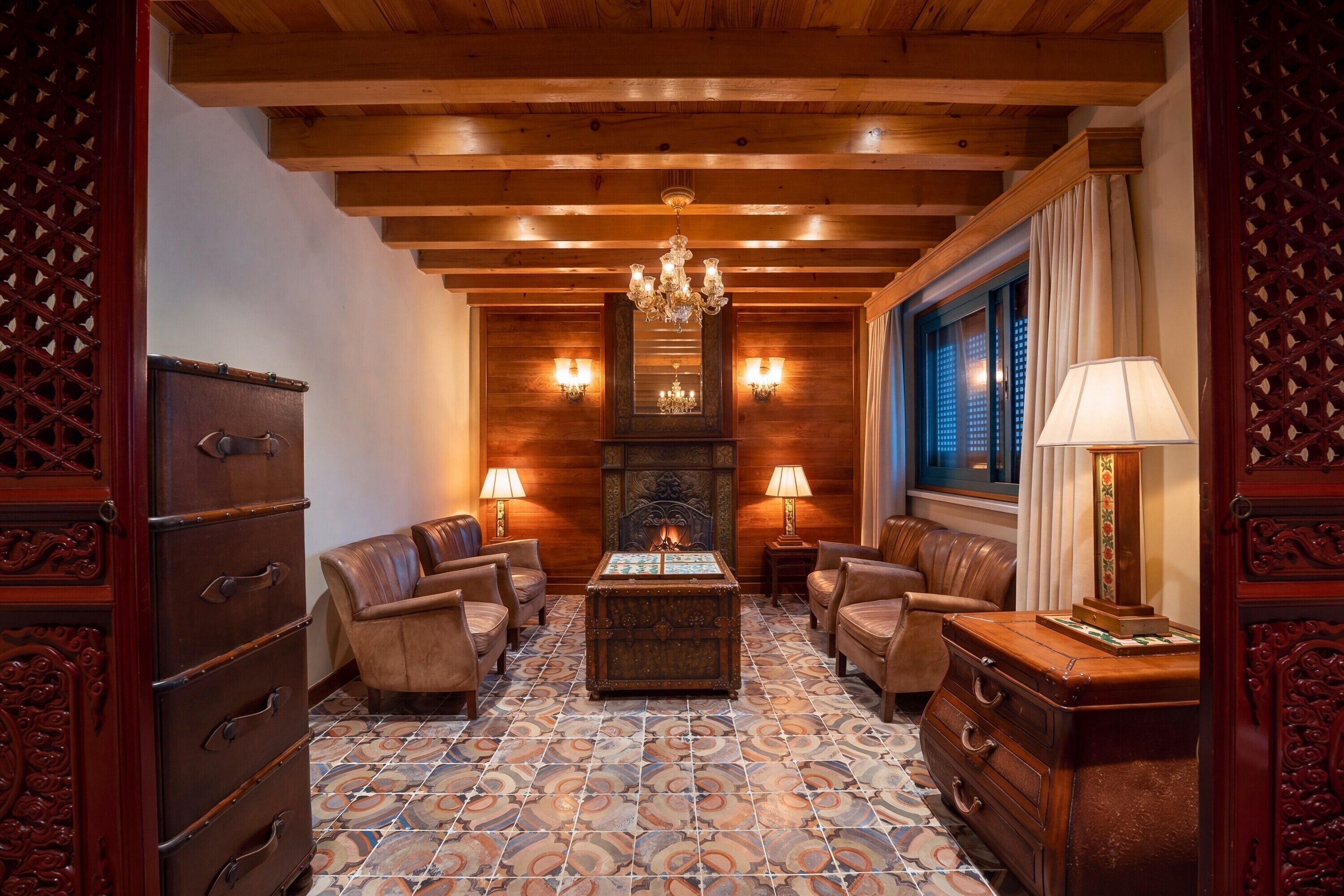 A room with a fireplace, leather sofas, a wooden chest, and a patterned floor.
