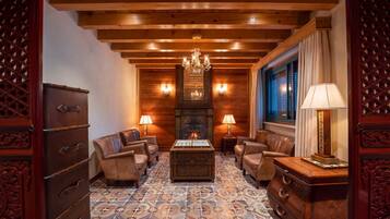 A room with a fireplace, leather sofas, a wooden chest, and a patterned floor.