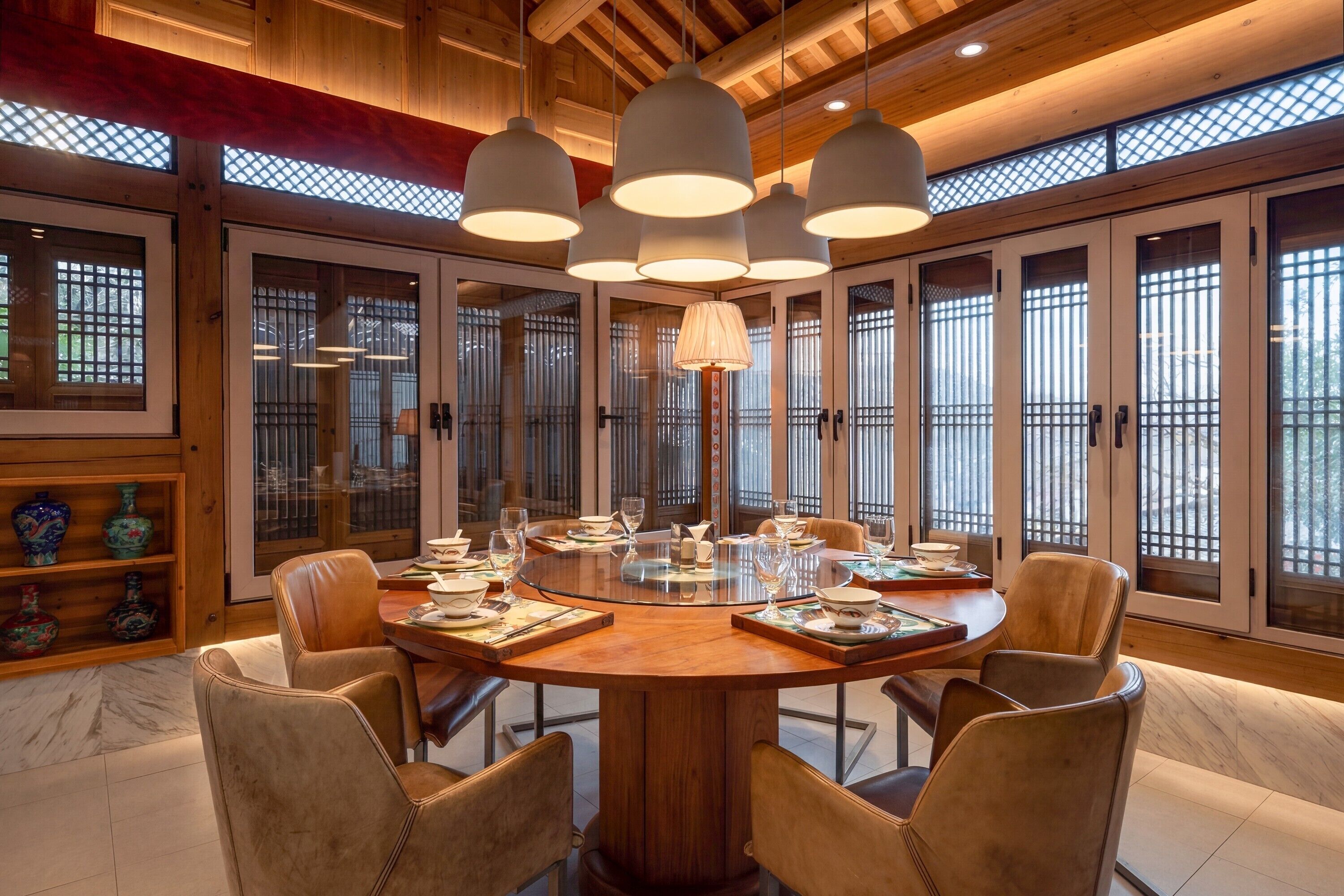 Une table de salle à manger ronde, entourée de chaises, un lustre et des fenêtres de style traditionnel avec des grilles.