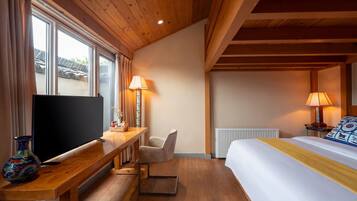 Habitación de hotel con techo de madera, cama con colcha amarilla, escritorio con televisor, una silla y dos lámparas.