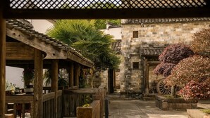 A courtyard with a wooden pergola, stone walls, and a large wheel.