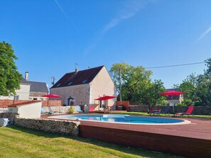 Ett hus med en swimmingpool, stenmurar och röda parasoller.