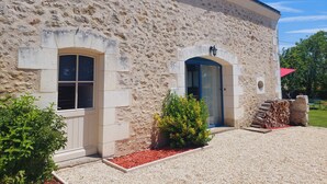 A stone building with a door and windows, a small garden area with gravel and plants, and a stack of firewood. - Le colibri - Country house with private pool (Chambourg-sur-Indre)