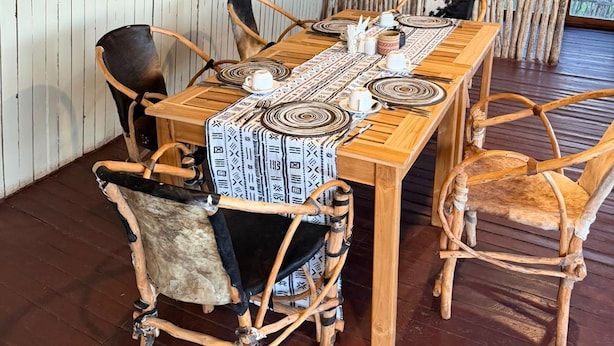 A wooden dining table with a patterned tablecloth, surrounded by rustic chairs. - Amani Eserian Ngorongoro (Ngorongoro)