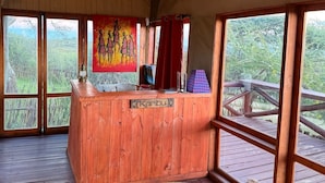 A wooden reception desk with a sign reading 'Karibu,' large windows with a view of greenery, and a woven mat on the floor. - Amani Eserian Ngorongoro (Ngorongoro)