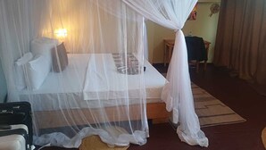 A room with a bed under a white canopy, a bedside table, a lamp, and a chair. - Amani Eserian Ngorongoro (Ngorongoro)